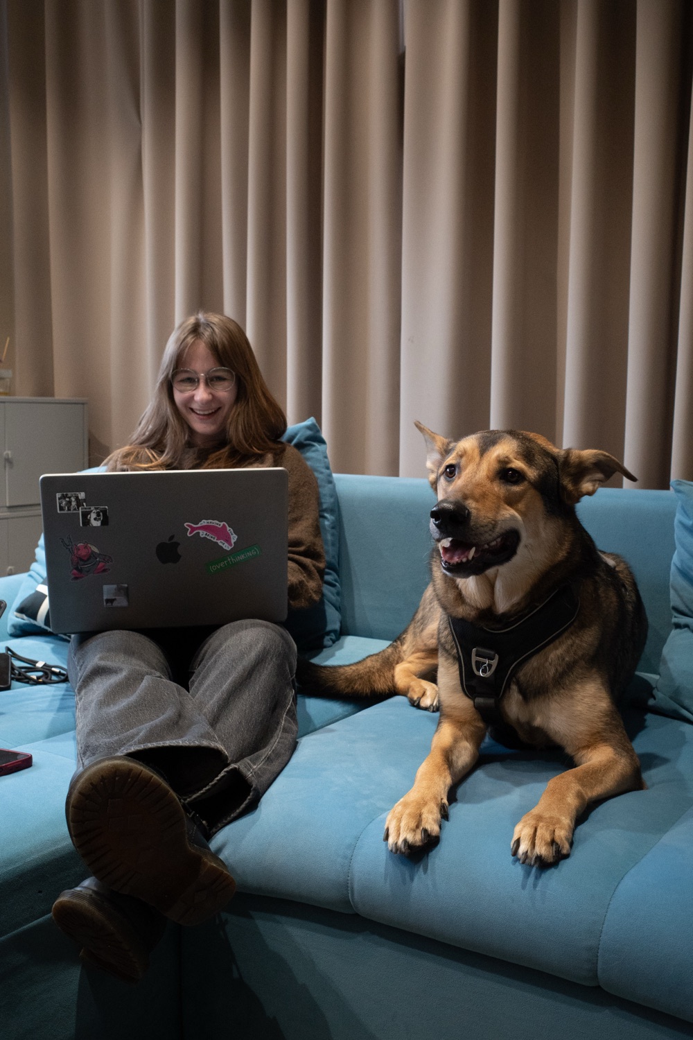 Anastasiia working on a laptop on a blue sofa next to a dog